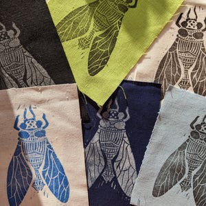 May include: Six fabric squares with different colored backgrounds and printed images of cicadas. The cicadas are printed in black, white, blue, and gray.