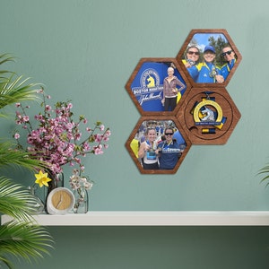Puede incluir: Un expositor de fotos hexagonal de madera con cuatro fotos de personas corriendo un maratón y una medalla con un logotipo de lobo. Las fotos están en marcos marrones con fondo blanco. La medalla está en un marco marrón con fondo blanco. El expositor está en una estantería blanca.