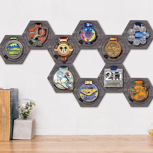 Puede incluir: Un expositor hexagonal gris para medallas con ocho soportes para medallas. Los soportes para medallas están dispuestos en forma de panal. Las medallas son de varios colores y diseños.