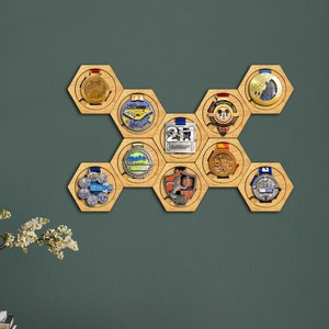 Puede incluir: Un expositor de medallas hexagonal de madera con 10 soportes para medallas. El expositor está montado en una pared verde. Las medallas son de varios colores y diseños.