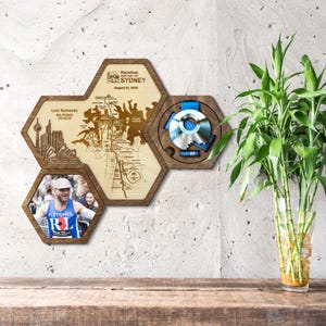 May include: Wooden hexagon-shaped display featuring a marathon map, a photo, and a medal. The map is of Sydney, Australia, with the text "Marathon Run Day of Sydney August 31, 2025." The photo shows a runner. The medal is blue and silver.