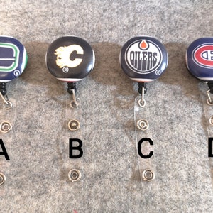 Peut inclure: Quatre porte-badges rétractables avec logo d'équipe de hockey. Les logos sont ceux des Canucks de Vancouver, des Flames de Calgary, des Oilers d'Edmonton et du Canadien de Montréal. Chaque porte-badge est doté d'une sangle en plastique transparente avec trois anneaux métalliques.