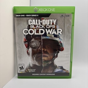 May include: A green plastic Xbox One game case for Call of Duty Black Ops Cold War. The cover art features a split-face soldier wearing sunglasses and a helmet with American flag patterns. It includes 4K Ultra HD, HDR, and ESRB Mature 17+ labels.