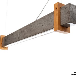 May include: A modern concrete and wood pendant light fixture with a rectangular shape and a built-in light source.