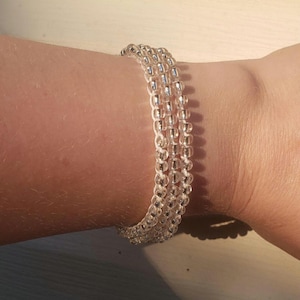 May include: A multi-strand bracelet featuring three rows of small, clear, translucent glass beads strung on a white cord. The beads have a reflective, shiny finish that catches the light, creating a simple and uniform appearance around the wrist.