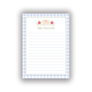 May include: A rectangular notepad featuring a light blue and white gingham border. The center contains horizontal lines for writing, topped with a watercolor illustration of a stack of books, two red apples, and the text MRS. WILLIAMS.
