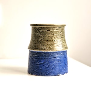 May include: A ceramic vase with a textured finish. The top half is a light brown colour and the bottom half is a dark blue colour.