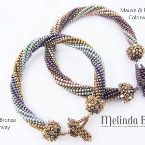 Könnte beinhalten: Zwei Perlenarmbänder, eines in Blau und Bronze, das andere in Mauve und Lila, mit dem Text "Melinda Barta" darunter.