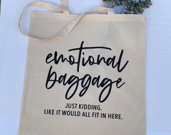 May include: A beige canvas tote bag with black text that reads "emotional baggage just kidding. like it would all fit in here."