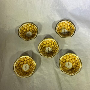 Peut inclure: Cinq petits bols ronds en métal blanc avec une bordure dorée. Chaque bol est rempli d'arachides jaunes et présente une image de personnage de cacahuète en dessin animé au centre.