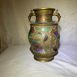 May include: An antique brass vase with intricate floral and dragon designs in red, blue, and green enamel. The vase features two ornate handles and a detailed base, showcasing a blend of artistry and craftsmanship.