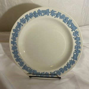 May include: A white ceramic dinner plate with a blue floral design around the rim. The plate is on a white surface.