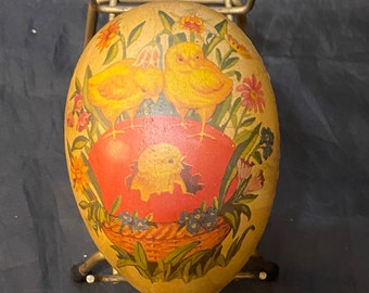 May include: A vintage Easter egg with a painted design of two yellow chicks and a lamb in a basket. The egg is on a gold metal stand.