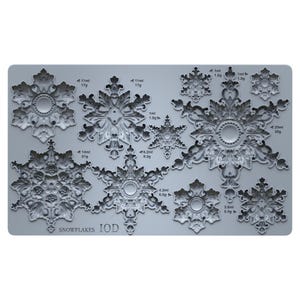 May include: A light gray silicone mold featuring various snowflake designs with intricate filigree patterns. The mold includes text labels for volume and weight in ml and g for each shape, with the text SNOWFLAKES IOD printed at the bottom.