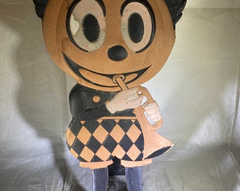 Puede incluir: Una decoración de Halloween vintage de cartón de un personaje con cabeza de calabaza tocando la trompeta. El personaje lleva un atuendo a cuadros blanco y negro, un sombrero negro y tiene una nariz y ojos negros.