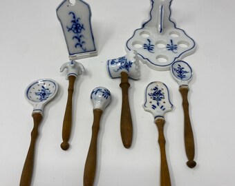 May include: A collection of antique porcelain kitchen tools with wooden handles. The white porcelain pieces feature blue floral designs. The tools include a spoon, a hammer, and a spatula. The handles are a dark brown color.