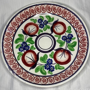 Peut inclure: Une assiette en céramique blanche avec un motif floral rouge et bleu. L'assiette a un centre blanc avec un anneau bleu autour. Le motif floral présente des fleurs rouges et blanches avec des feuilles vertes.