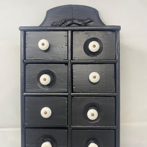 May include: Black wooden cabinet with eight drawers and white knobs. A squirrel figurine is on top of the cabinet. The cabinet is painted black and has a rustic, handmade appearance.