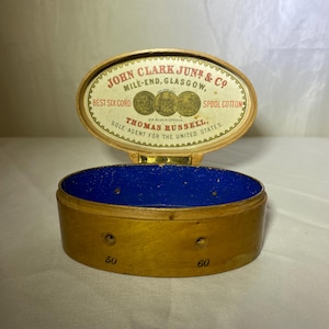 May include: An antique wooden spool cotton box with a hinged lid. The lid features text that reads "JOHN CLARK JUNR & CO" and "BEST SIX CORD SPOOL COTTON." The interior is lined with blue fabric. The box is marked with the numbers "50" and "60".