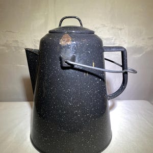 Puede incluir: Cafetera de camping de esmalte negro con un diseño blanco moteado y un asa de alambre.