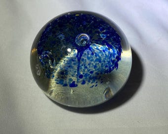 May include: A clear glass paperweight, spherical in shape. The interior has a vibrant blue design with a speckled pattern and air bubbles, creating a unique decorative piece. The paperweight is a decorative item.