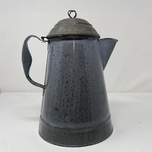 May include: A vintage, speckled blue enamelware coffee pot with a dark metal lid and handle. The pot has a spout for pouring and a rounded body. The handle is attached to the side of the pot. The pot is likely used for brewing coffee.