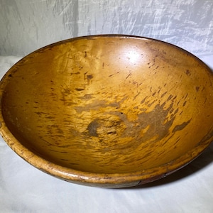 May include: A large, wooden bowl with a natural, light brown finish. The bowl has a wide, rounded shape and shows signs of wear and use.