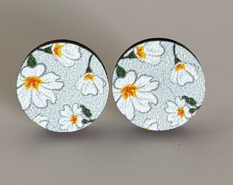 Könnte beinhalten: Ein Paar runde Holzohrringe mit weißem Hintergrund und einem floralen Muster aus kleinen weißen Blüten mit gelben Zentren.
