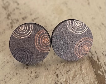 Könnte beinhalten: Ein Paar runde Ohrstecker in Grau mit einem wirbelnden Muster in Weiß und Kupfer.