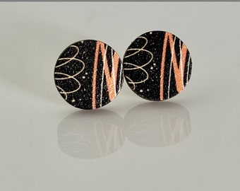 Könnte beinhalten: Ein Paar runde Ohrstecker in Schwarz und Gold mit einem abstrakten Design in Weiß und Rosa.