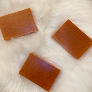 May include: Three rectangular bars of orange soap on a white fluffy surface.