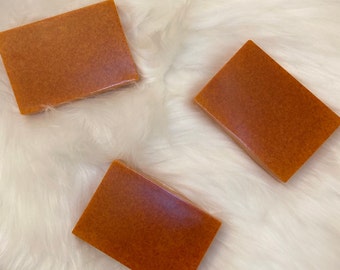 May include: Three rectangular bars of orange soap on a white fluffy surface.