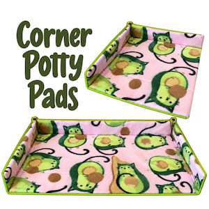 May include: Corner Potty Pads with a light pink background featuring a repeating pattern of green avocado cats with brown pits. The rectangular and corner-shaped fabric pads have bright lime green trim along the edges.