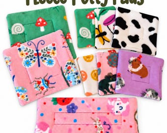 May include: A collection of square and rectangular fleece potty pads featuring various colorful prints including butterflies, mushrooms, cow spots, frogs, and small animals, with the text Fleece Potty Pads displayed at the top.