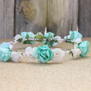 Peut inclure: Une couronne de fleurs blanche et turquoise avec un ruban de satin blanc. La couronne est faite de fleurs et de verdure artificielles.