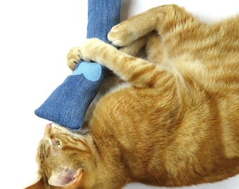 May include: A ginger cat playing with a blue denim cat toy with a blue heart on it.