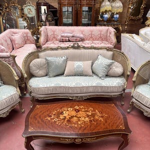 May include: A collection of antique furniture, including sofas, chairs, and a coffee table. The sofas have ornate frames and patterned upholstery in shades of pink and beige. The coffee table features a floral inlay design.