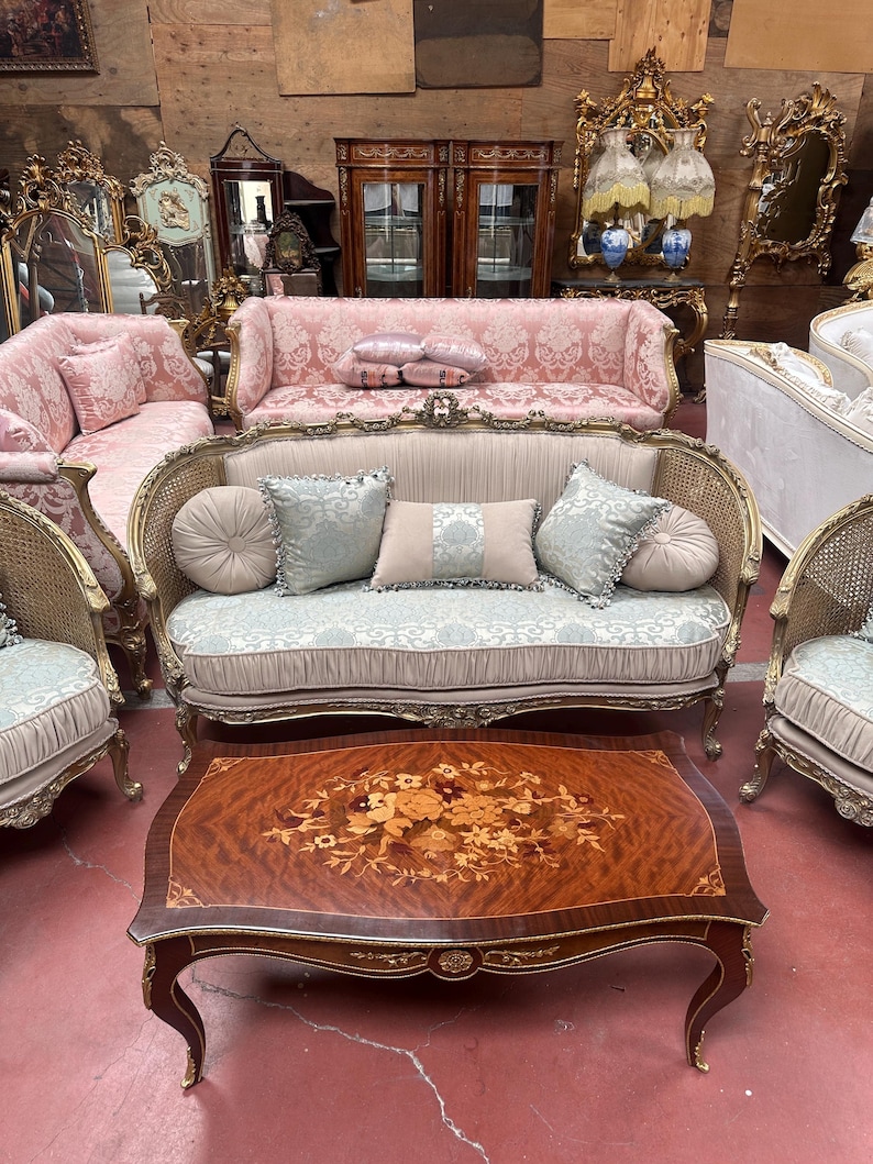 May include: A collection of antique furniture, including sofas, chairs, and a coffee table. The sofas have ornate frames and patterned upholstery in shades of pink and beige. The coffee table features a floral inlay design.