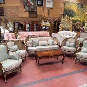 May include: A collection of antique furniture, including sofas, armchairs, and a coffee table. The pieces feature ornate gold frames, light blue patterned upholstery, and decorative pillows. The coffee table has a dark wood finish with an inlaid floral design.