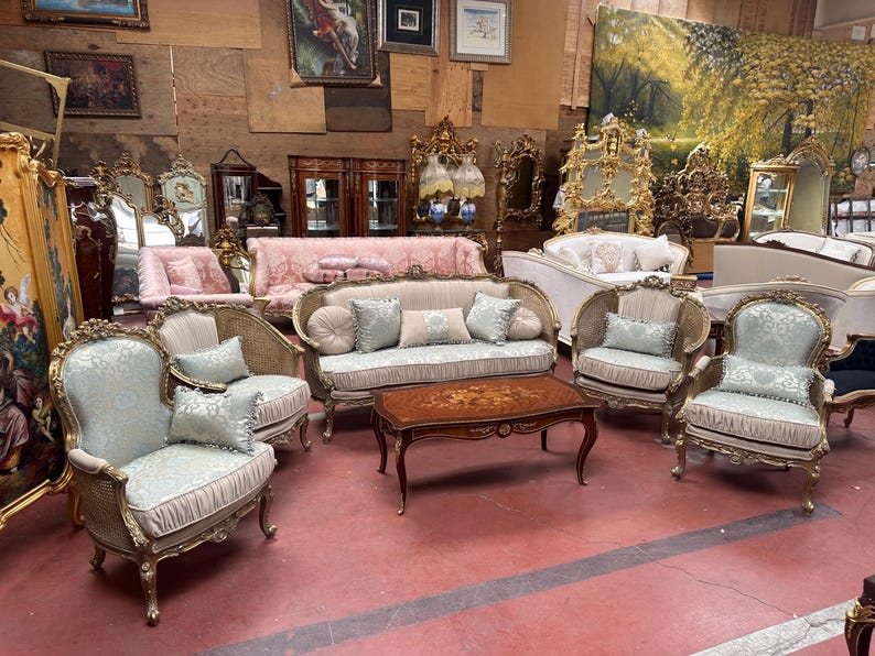 May include: A collection of antique furniture, including sofas, armchairs, and a coffee table. The pieces feature ornate gold frames, light blue patterned upholstery, and decorative pillows. The coffee table has a dark wood finish with an inlaid floral design.