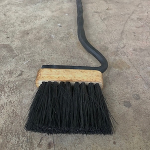 Puede incluir: Un atizador de chimenea de metal negro con un mango de cabeza de caballo y un cepillo de madera unido al extremo.