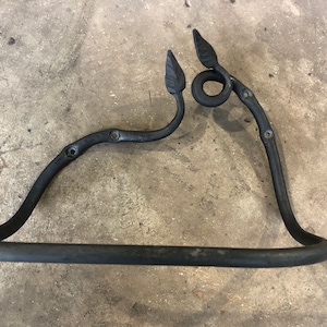 Puede incluir: Toallero de metal negro con extremos en forma de hoja y un adorno en espiral. El toallero está diseñado para ser montado en una pared.