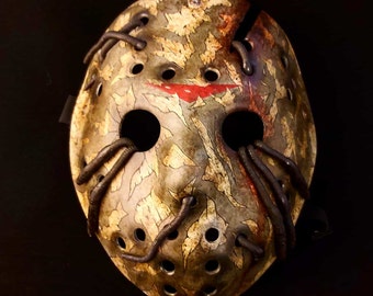 May include: A hockey mask with a camouflage pattern, red paint splatters, and black straps. The mask has a distressed look and is made of plastic.