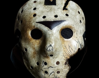 May include: A white hockey mask with black straps and a black painted design. The mask has a cracked and weathered appearance, with holes throughout the surface.