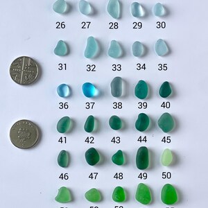 Puede incluir: Una variedad de vidrios marinos en tonos aguamarina, turquesa y verdes, numerados del 26 al 56. Dos monedas se colocan junto al vidrio marino para comparar el tama&ntilde;o. El texto "Aquas, Teals and Greens" est&aacute; en la parte superior.