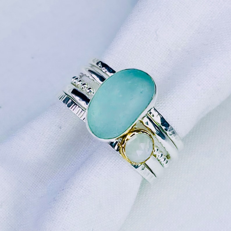 Puede incluir: Un conjunto de anillos de plata con una piedra ovalada azul claro y una piedra blanca redonda m&aacute;s peque&ntilde;a. Los anillos tienen detalles texturizados y con cuentas. Las piedras est&aacute;n sobre un fondo blanco.