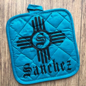 May include: Teal blue quilted hot pad with a black Zia symbol and the name "Sanchez" in black script.