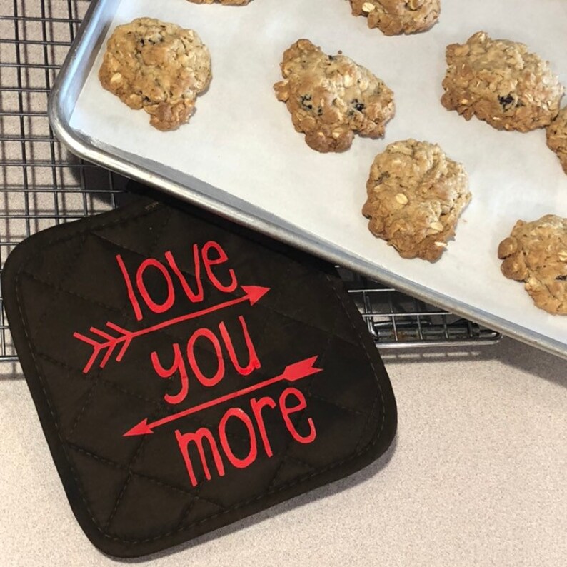 May include: A brown quilted hot pad with the text "love you more" in red lettering with arrows pointing to the text.