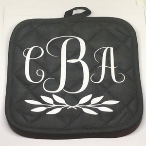 May include: Black quilted pot holder with a white monogram "CBA" and a white leafy design.