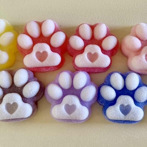 May include: A collection of colorful paw-shaped soaps. The soaps are in various colors, including green, yellow, red, pink, white, navy, brown, purple, blue, and light blue. Each paw has a heart-shaped detail.